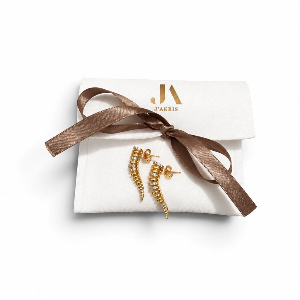 Jakris Zaria gold-plated brass earrings with sparkling zircon stones in a sculptural curved design on a gift pouch.