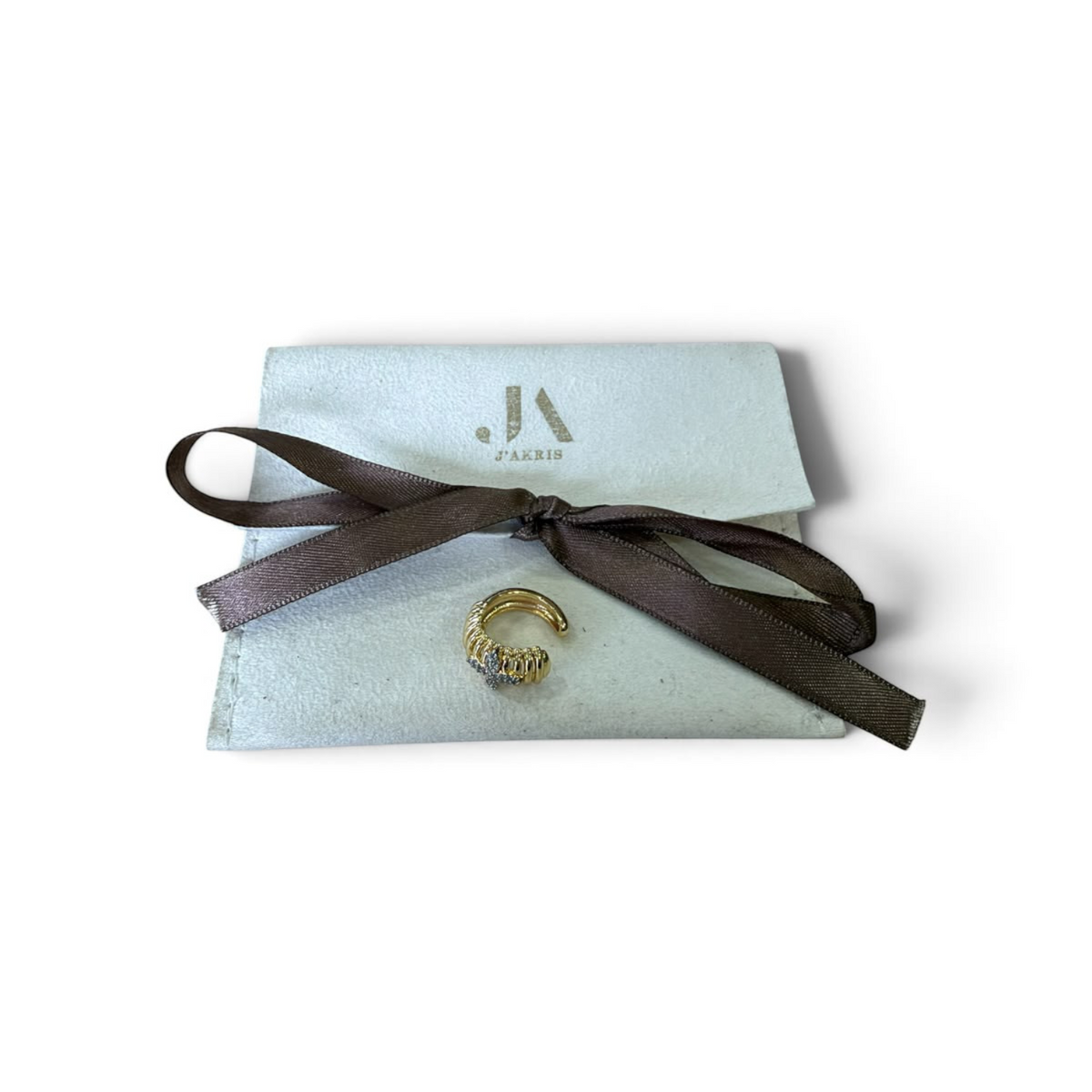 Jakris gold ear cuff with ridged design and four-leaf zircon stone detail, displayed on a branded white pouch.