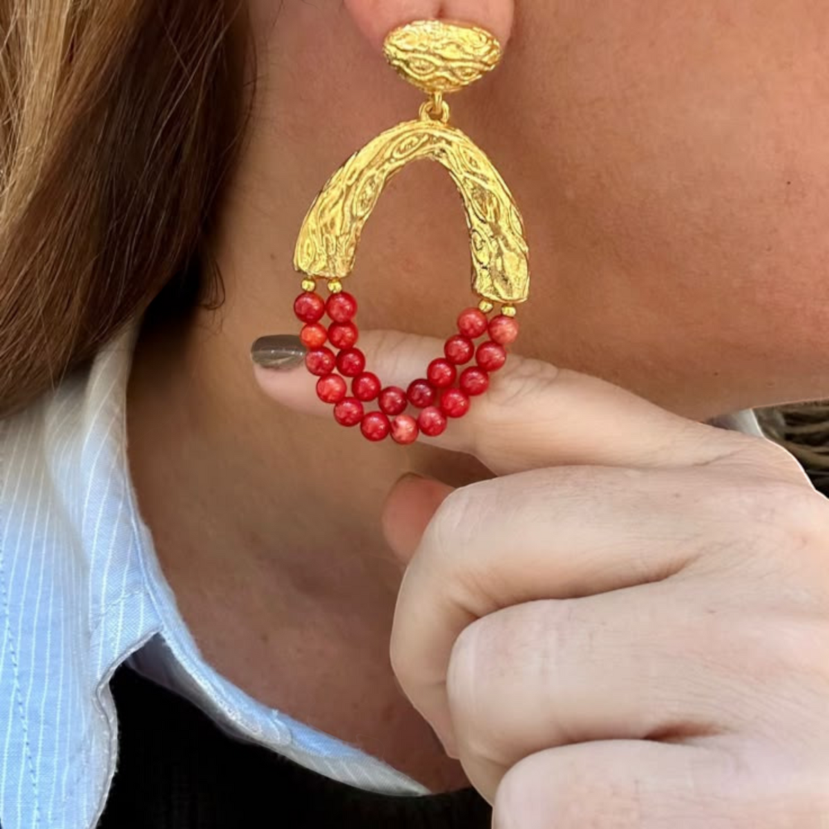 Jakris Rossa statement earrings featuring 24k gold-plated textured metal and vibrant red coral beads on a model.