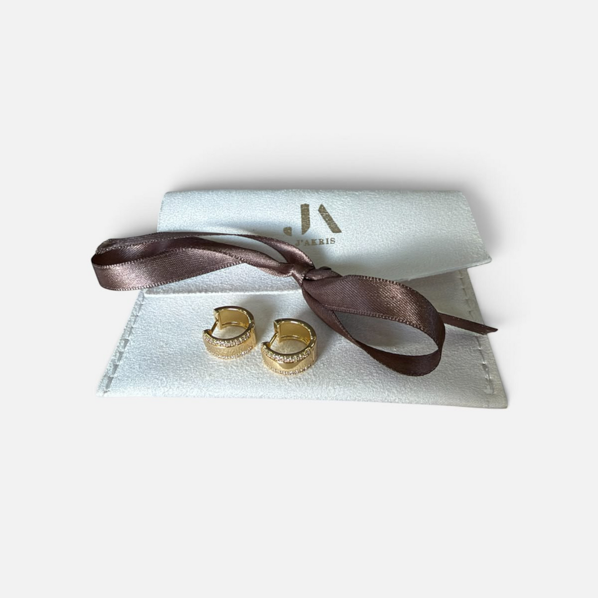 Jakris gold hoop earrings with sparkling zircon stones, displayed with a branded white pouch and brown ribbon.