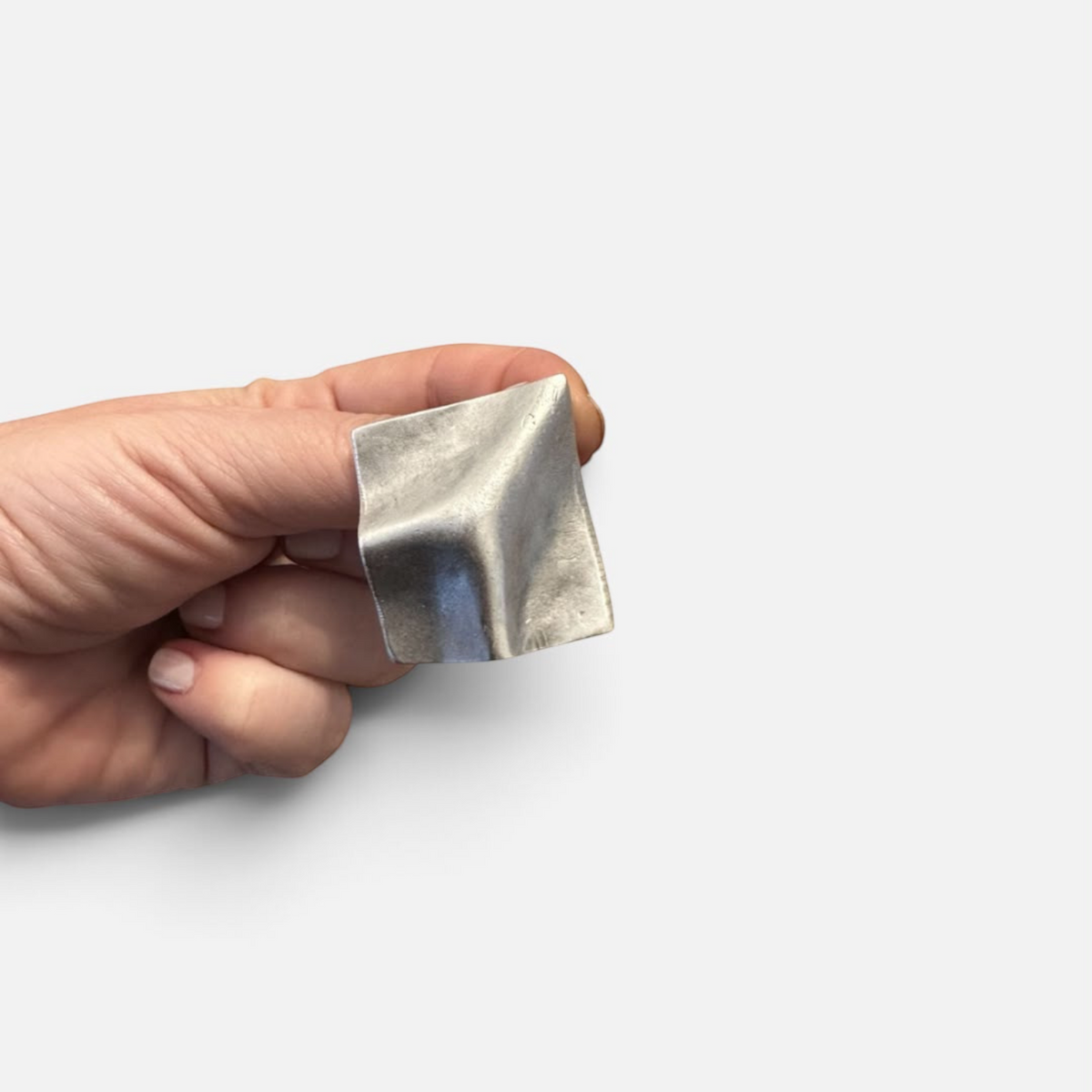 Jakris Noila sculptural silver-tone square earring with a curved, organic surface held in a hand.
