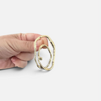 Jakris Alara gold plated abstract oval earring with textured surface held in hand