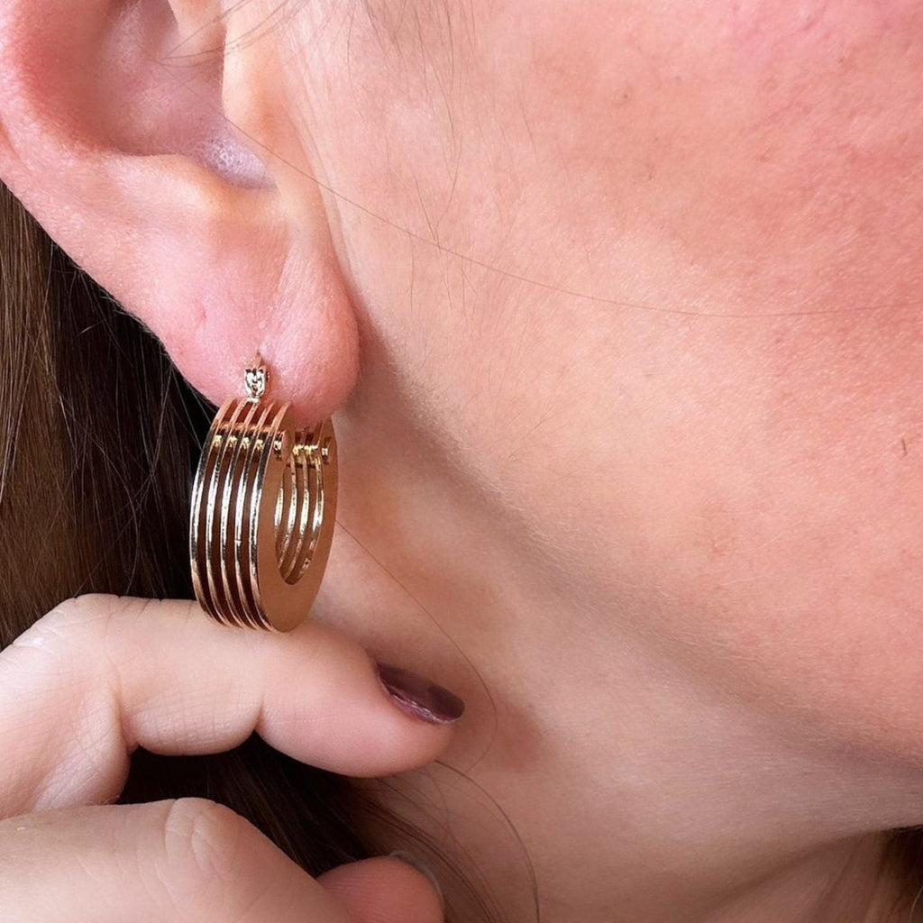 Jakris 5-layer thick gold hoop earring worn on a woman's ear, featuring a modern stacked design.