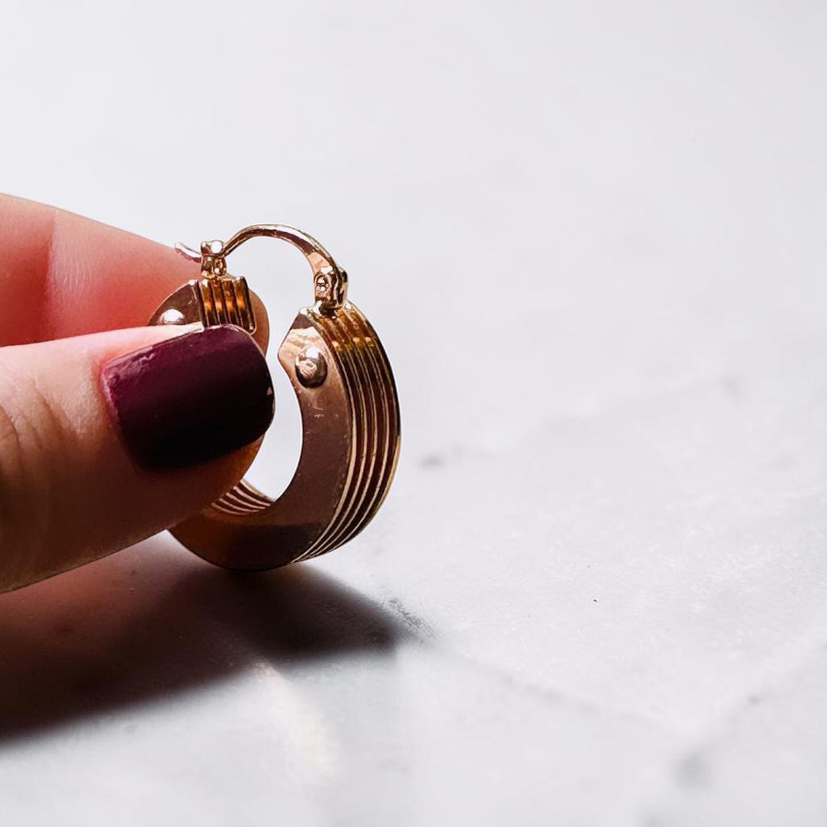 Jakris 5-layer thick gold hoop earring held by fingers against a white marble background