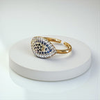 Jakris adjustable gold-tone ring featuring an evil eye motif adorned with sparkling blue and white zircon stones.