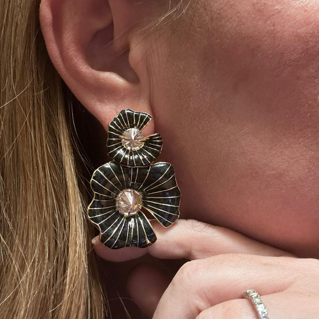Jakris black enamel flower earrings with central pearl detail worn on a woman's ear