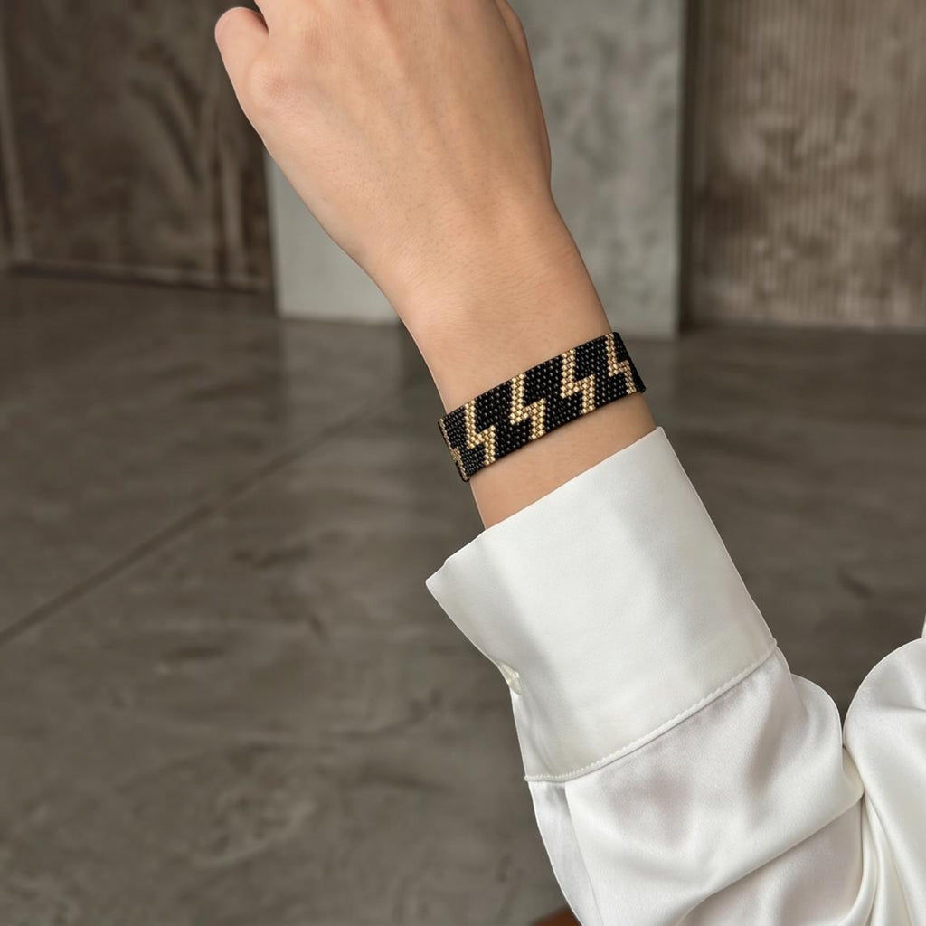 Jakris woven beaded bracelet featuring a black and gold lightning bolt pattern on a wrist