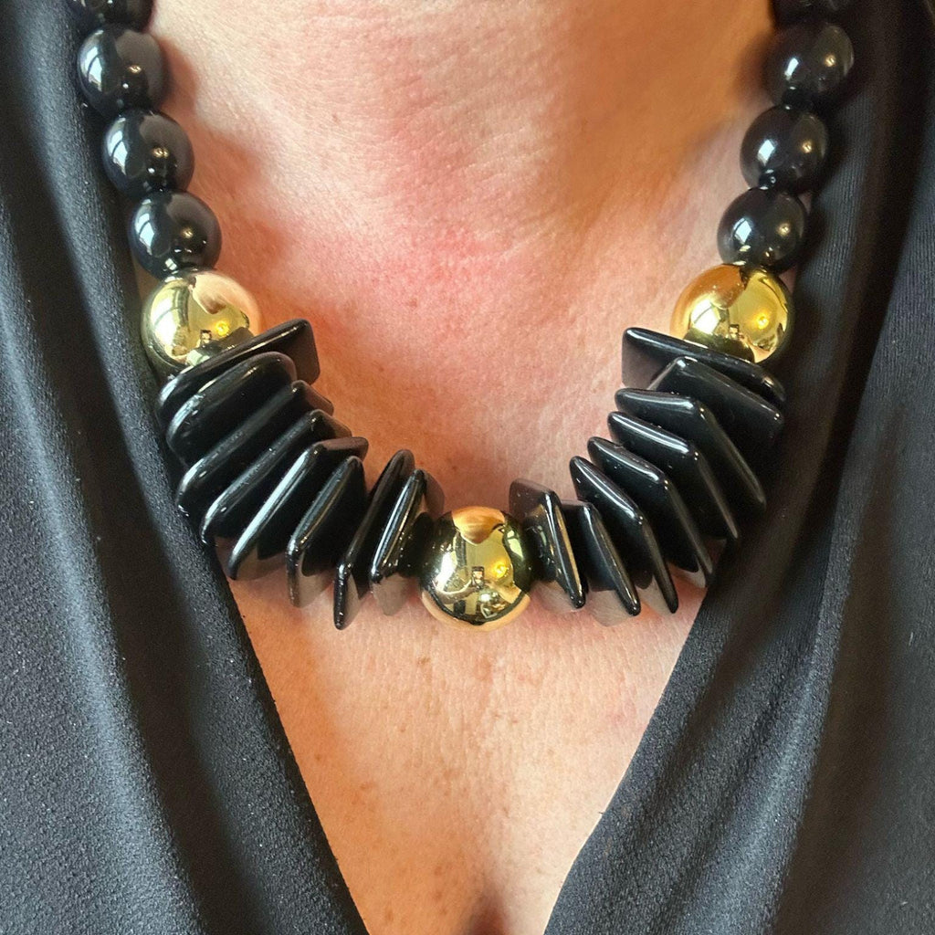 Jakris black and gold statement necklace featuring thick geometric beads and polished gold spheres on a model