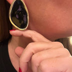 Jakris black oval earring with a gold-toned metallic rim worn on a woman's ear