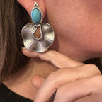 Jakris statement earrings featuring a blue stone and organic silver-plated brass design worn on a person's ear.