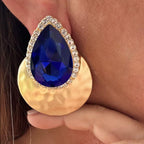 Jakris blue teardrop evening earring with a large crystal, gold hammered disc, and rhinestone border on a model