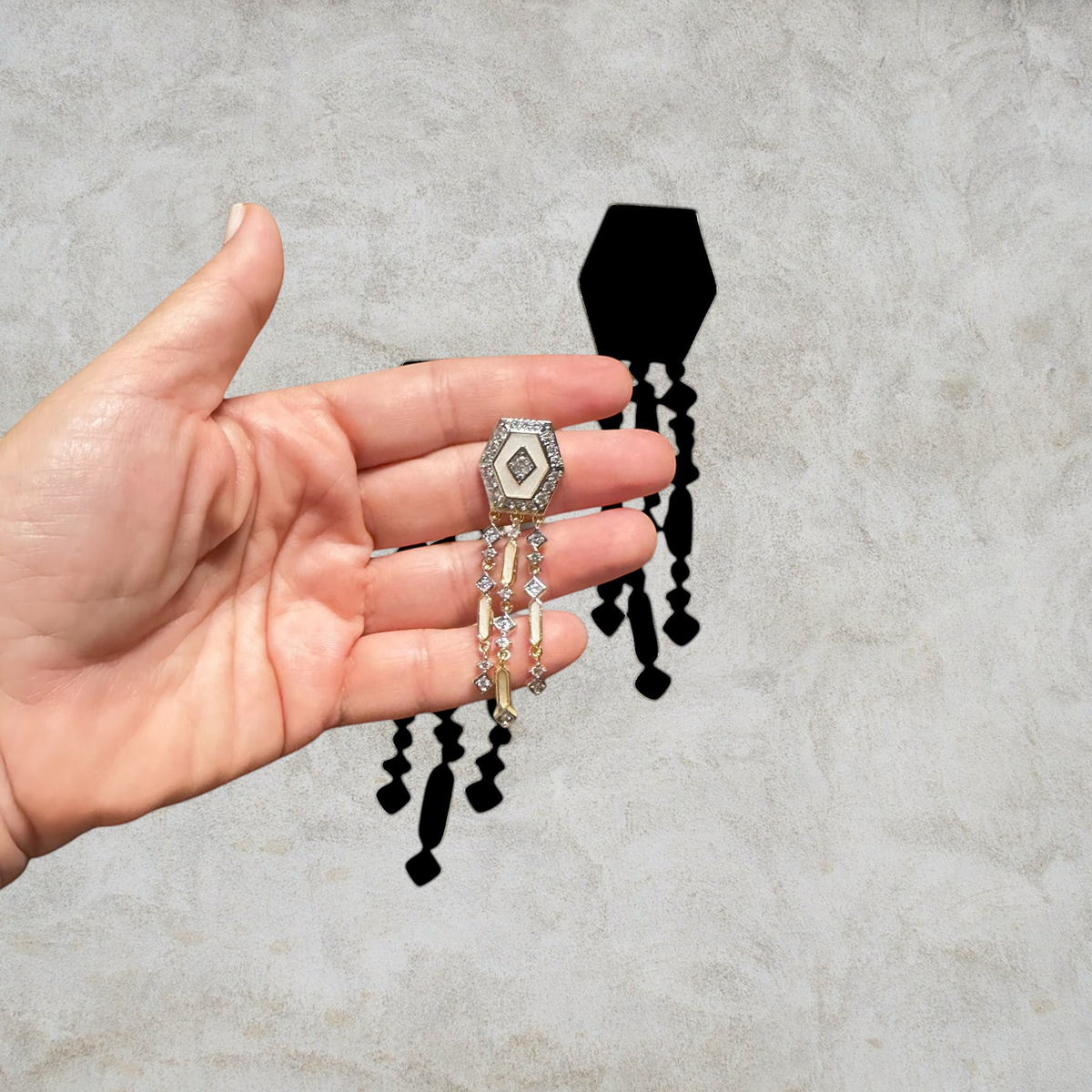 Jakris Elara gold-plated hexagonal drop earrings with sparkling zircon stones held in a hand.
