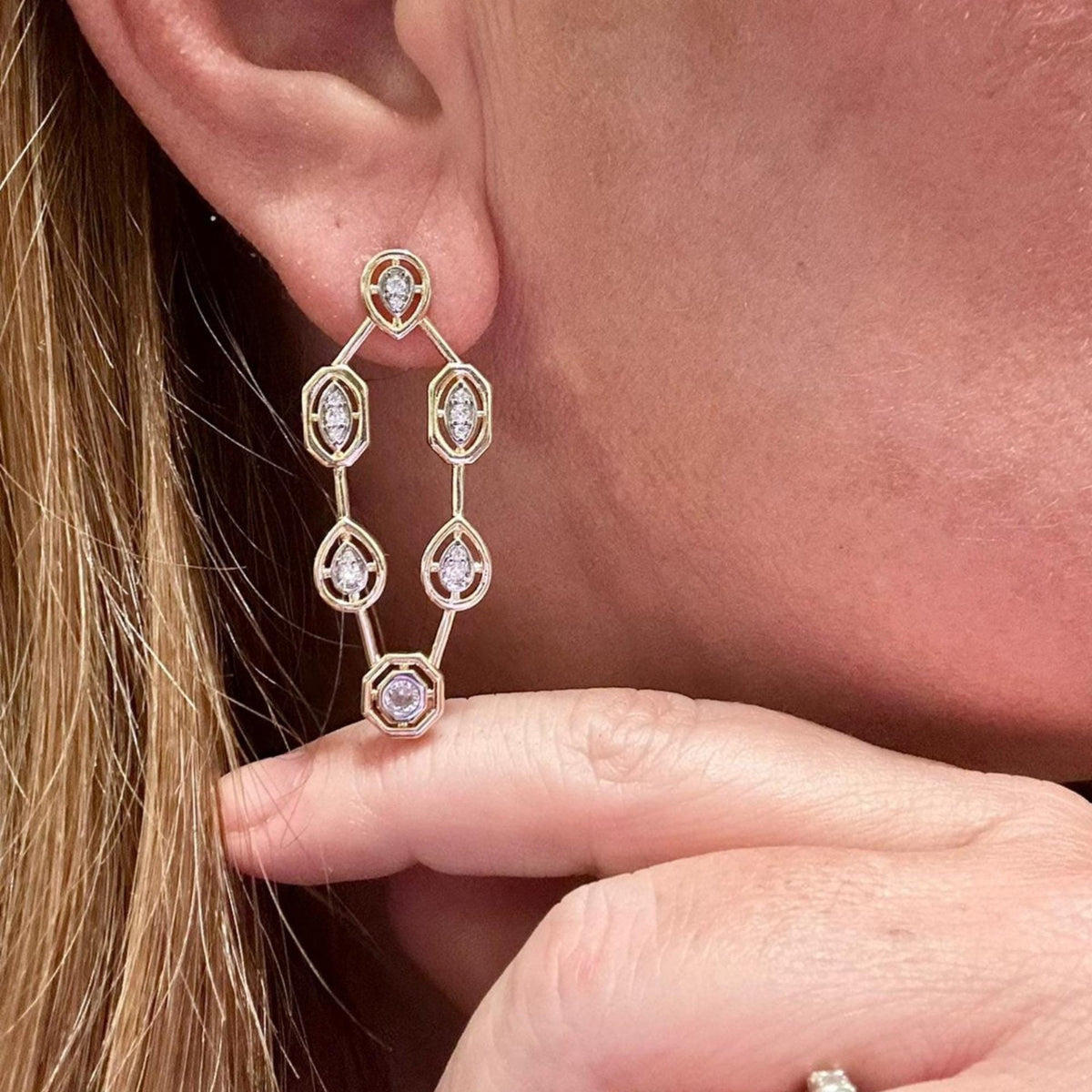Jakris geometric drop earrings featuring gold-tone metal and sparkling crystal accents worn on a woman's ear