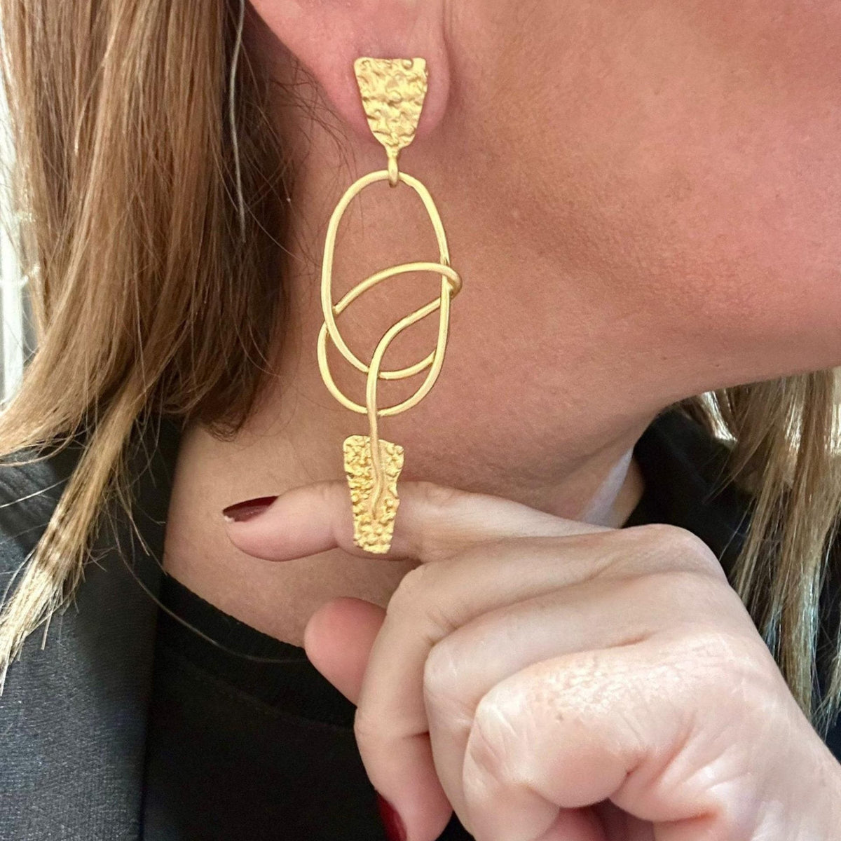 Jakris modern gold dangle earrings featuring abstract textured geometric shapes worn on a woman's ear