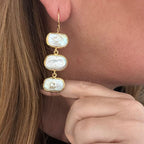 Jakris gold drop earrings featuring three rectangular baroque freshwater pearls worn on a woman's ear