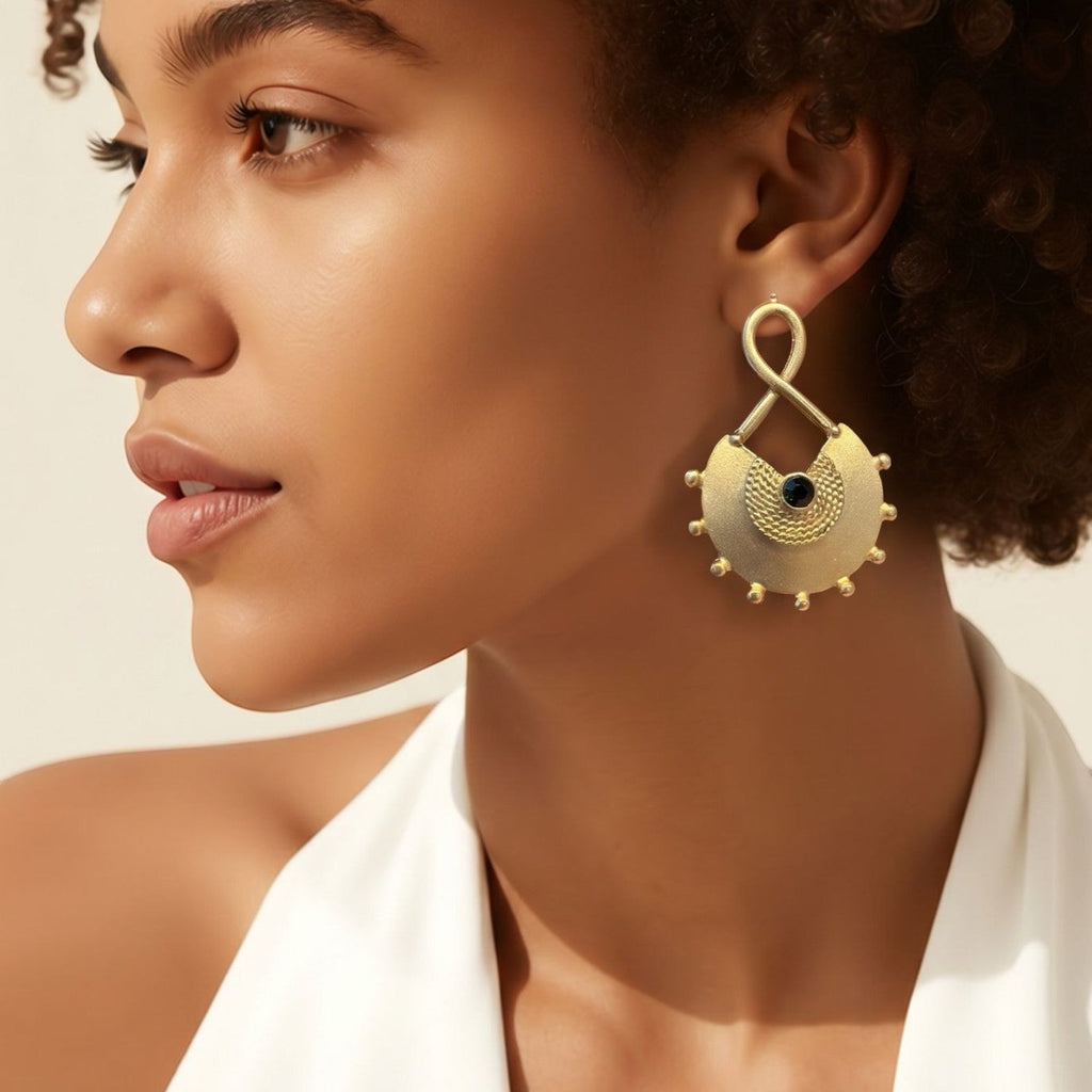 Jakris gold plated brass earring with a central black stone, textured round design, and beaded edge on a model.