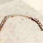 Jakris gold plated thick Cuban link chain necklace with crystal embellishments on a textured stone surface