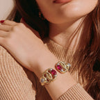 Jakris modern gold cuff bracelet featuring oval red and green gemstones worn by a woman in a beige sweater