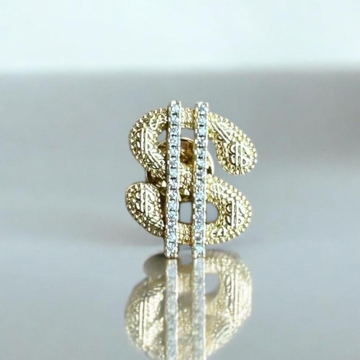 Jakris gold-tone dollar sign brooch featuring a textured surface and a vertical row of sparkling clear crystals.