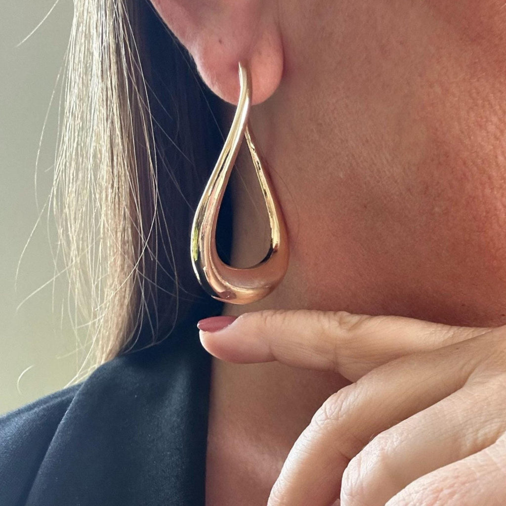 Jakris sculptural gold drop hoop earring worn on a woman's ear, featuring a modern, smooth, oversized teardrop design.