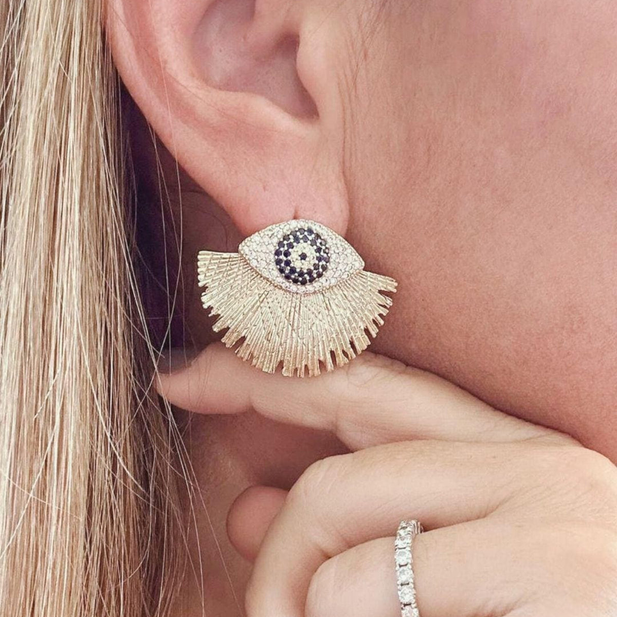 Jakris gold-plated evil eye fringe earrings with blue and white stone detailing worn on a model's ear