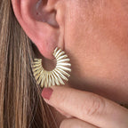 Jakris gold fan-shaped textured hoop earring worn on an earlobe, featuring a bold sunburst design.