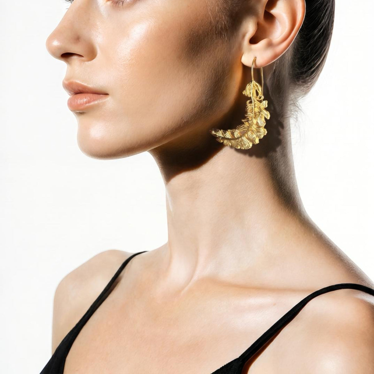 Jakris 24k gold plated feather shaped statement earring worn by a model in profile view