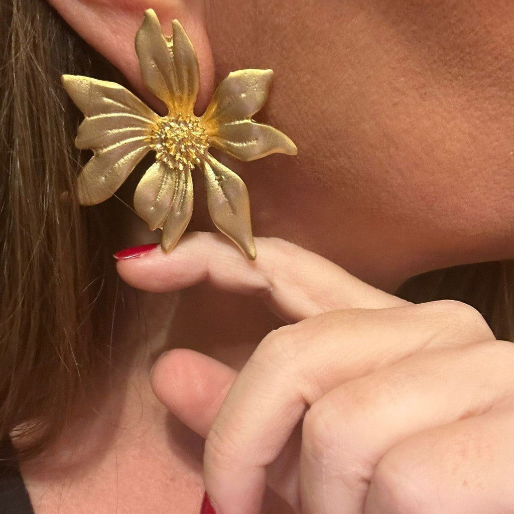 Jakris gold-plated flower-shaped statement earring worn on a woman's ear with textured petal details