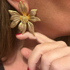 Jakris gold-plated flower-shaped statement earring worn on a woman's ear with textured petal details