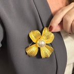 Jakris large gold-tone flower brooch with a central pearl accent pinned to a grey blazer