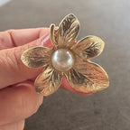 Jakris gold-plated textured flower earring with a central pearl detail held in hand