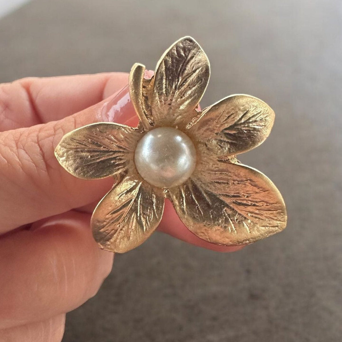 Jakris gold-plated textured flower earring with a central pearl detail held in hand