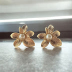 Jakris textured gold-plated flower earrings featuring a central pearl detail on a neutral surface.