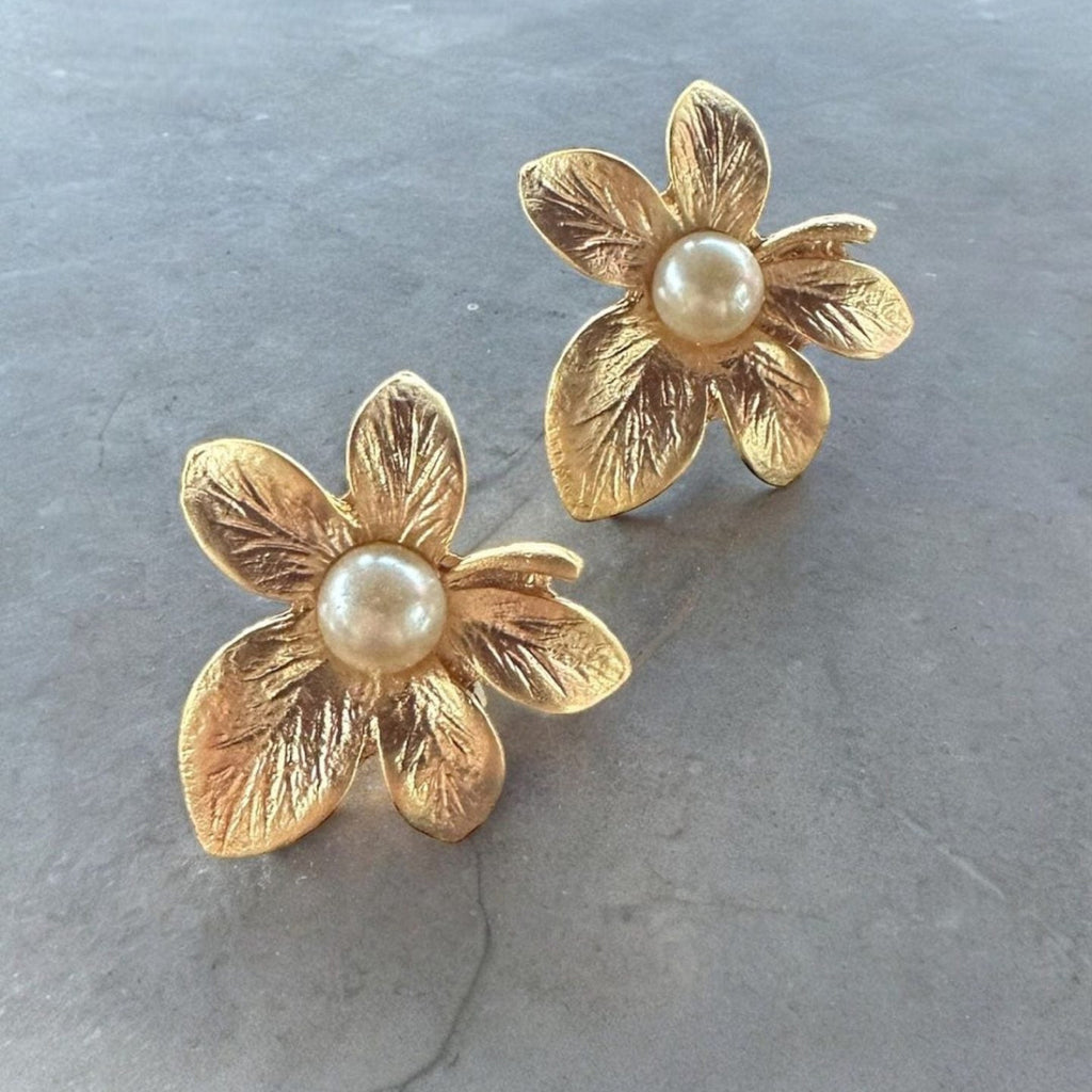 Jakris gold-plated textured flower earrings with central pearl detail on a grey surface
