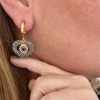 Jakris gold hoop earring featuring a heart-shaped pendant with blue crystal evil eye detailing worn on an earlobe