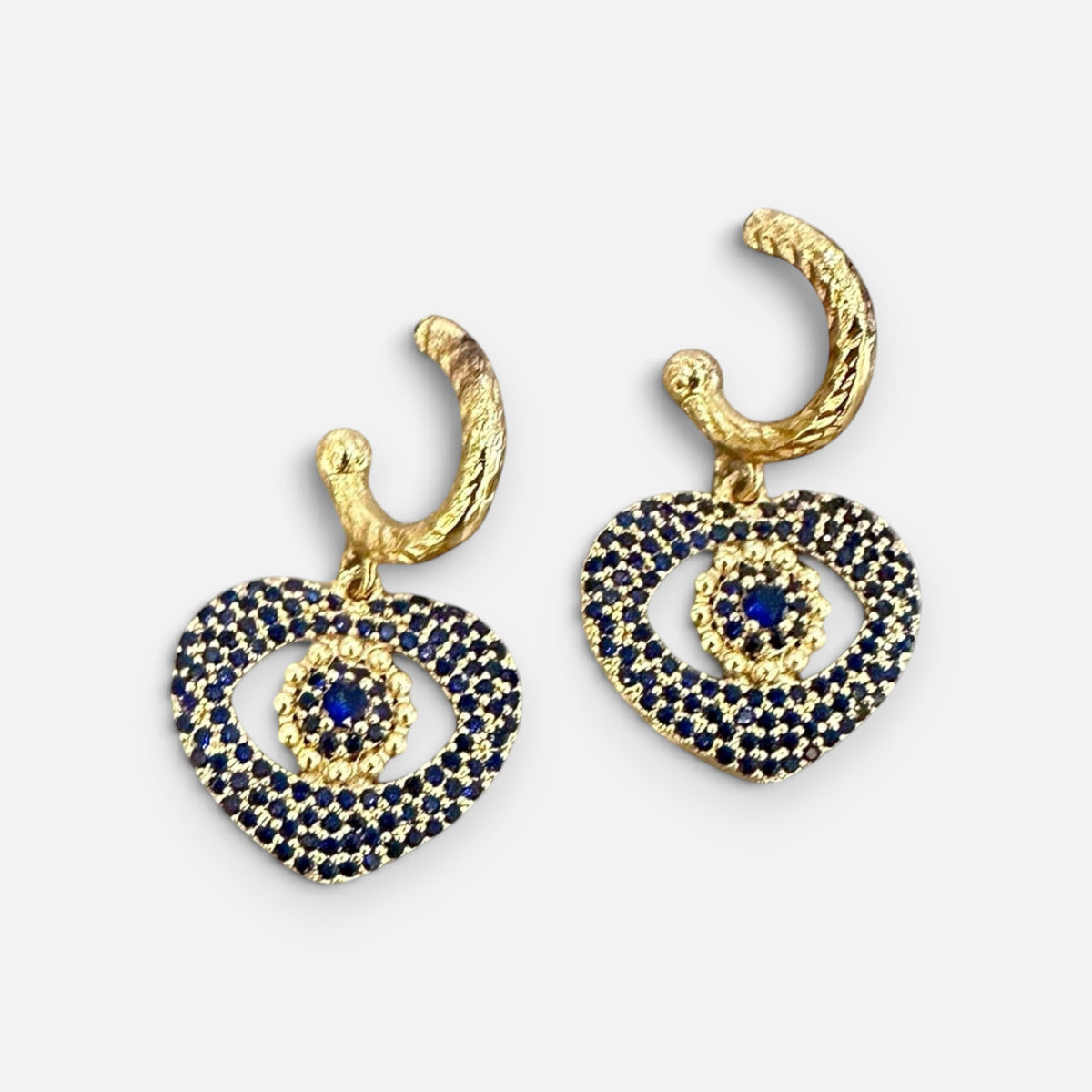 Jakris gold heart earrings featuring blue crystal evil eye details and textured hoop closures