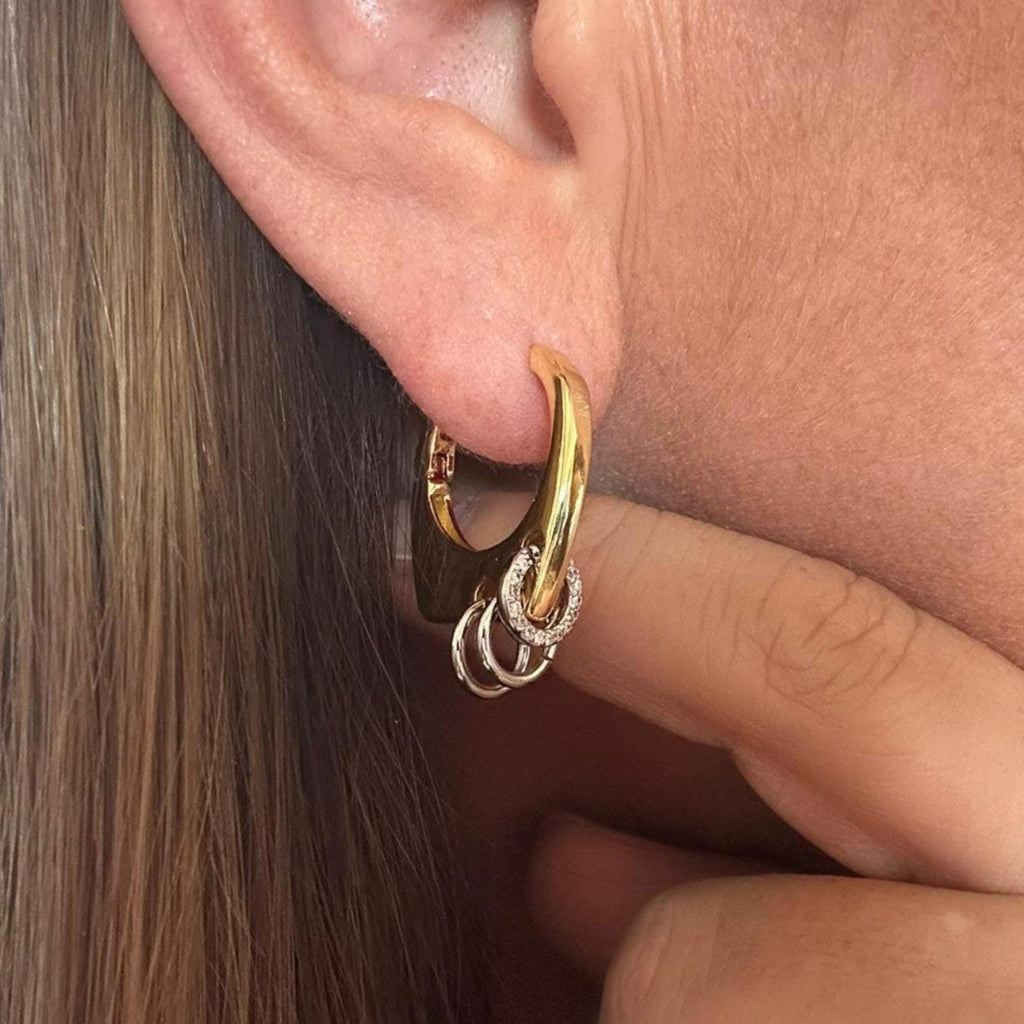 Jakris modern gold hoop earring featuring small silver-toned ring charms worn on an earlobe.