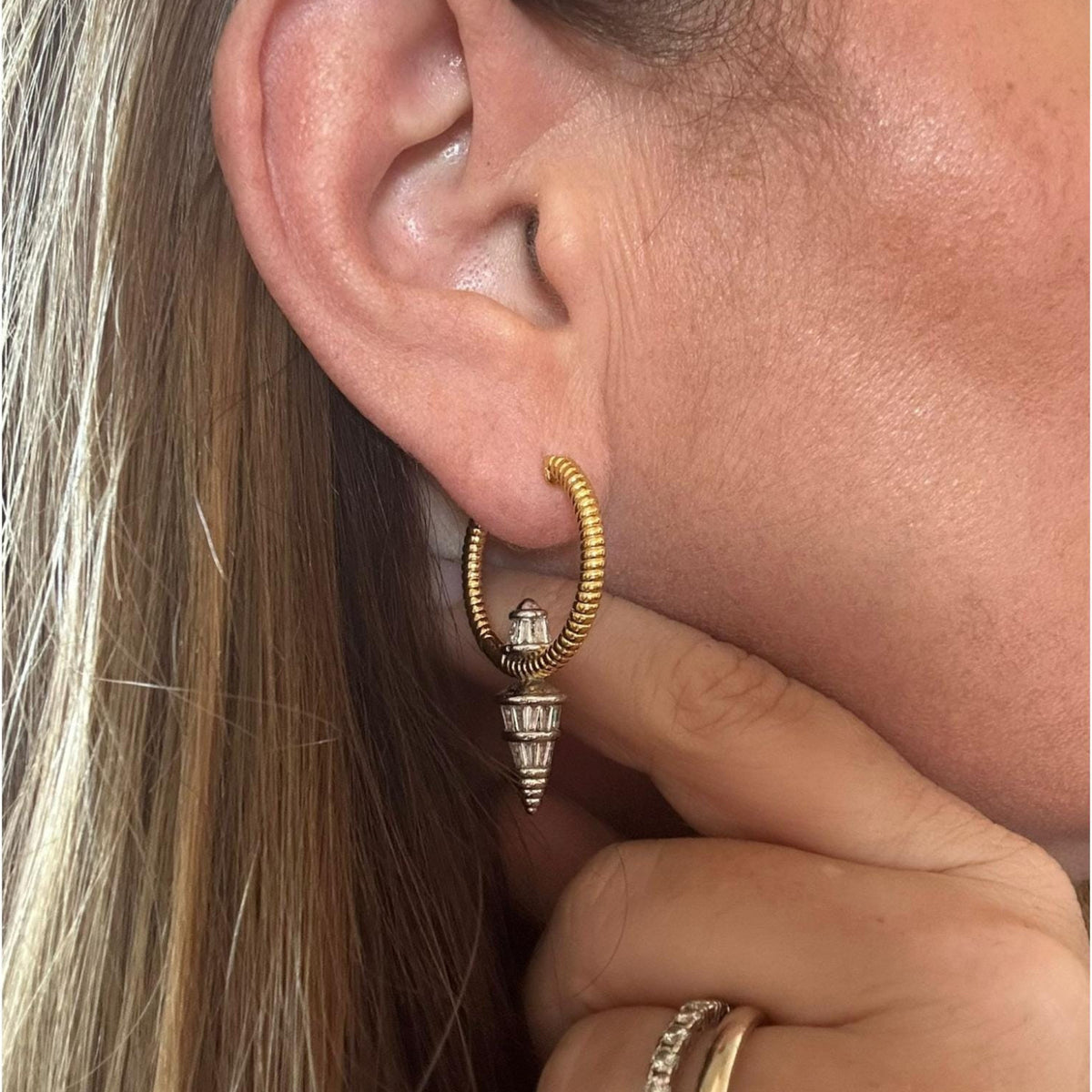 Jakris gold hoop earring with a silver pointed pendant featuring sparkling zircon stones worn on a woman's ear