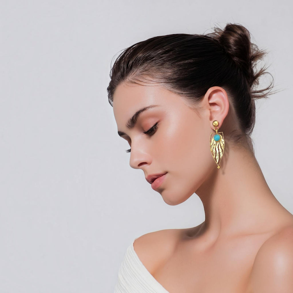 Jakris gold-plated leaf-shaped earrings with turquoise stone worn by a woman with hair in a bun