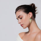 Jakris gold-plated leaf-shaped earrings with turquoise stone worn by a woman with hair in a bun