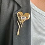 Jakris gold melted heart brooch with a square crystal accent pinned to a black blazer lapel