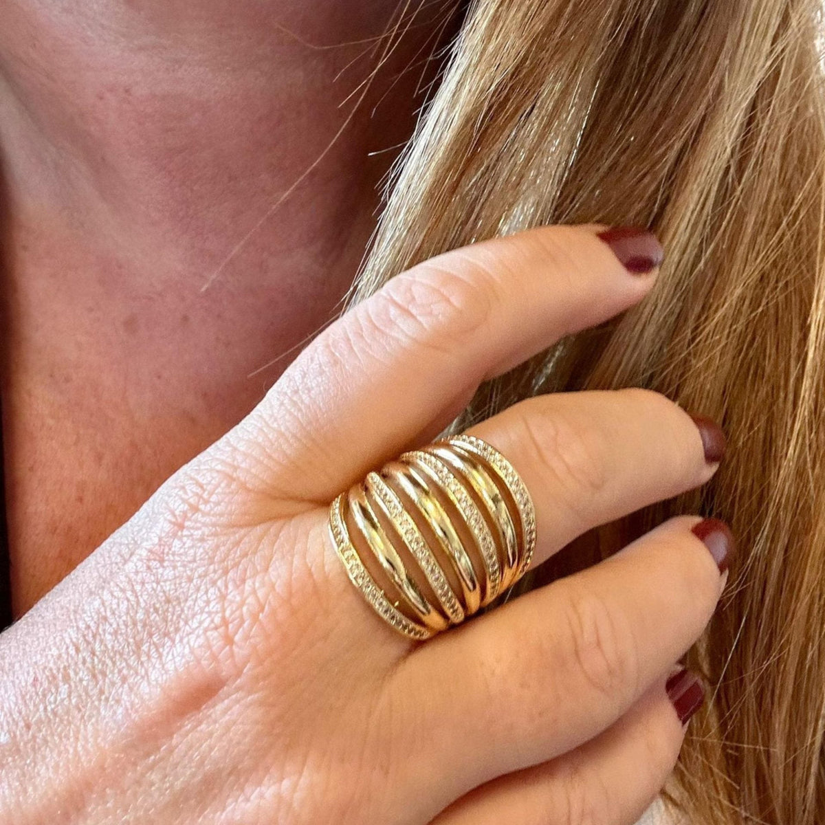 Jakris gold multi-band ring featuring sparkling crystal details worn on a finger with dark red nail polish