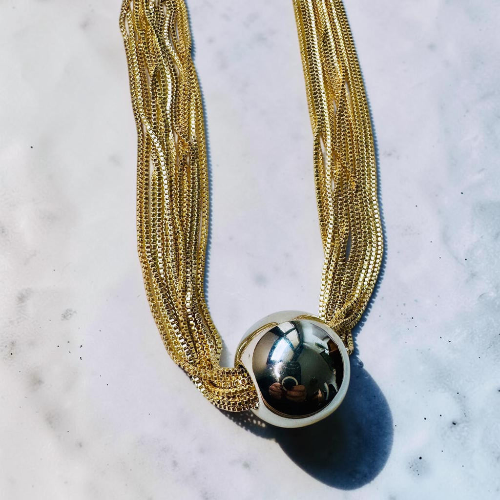 Jakris gold-toned multi-strand chain necklace featuring a large polished spherical ball pendant on a marble surface