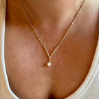 Jakris gold necklace featuring a delicate V-shaped chain with a single dangling pearl pendant worn on a woman
