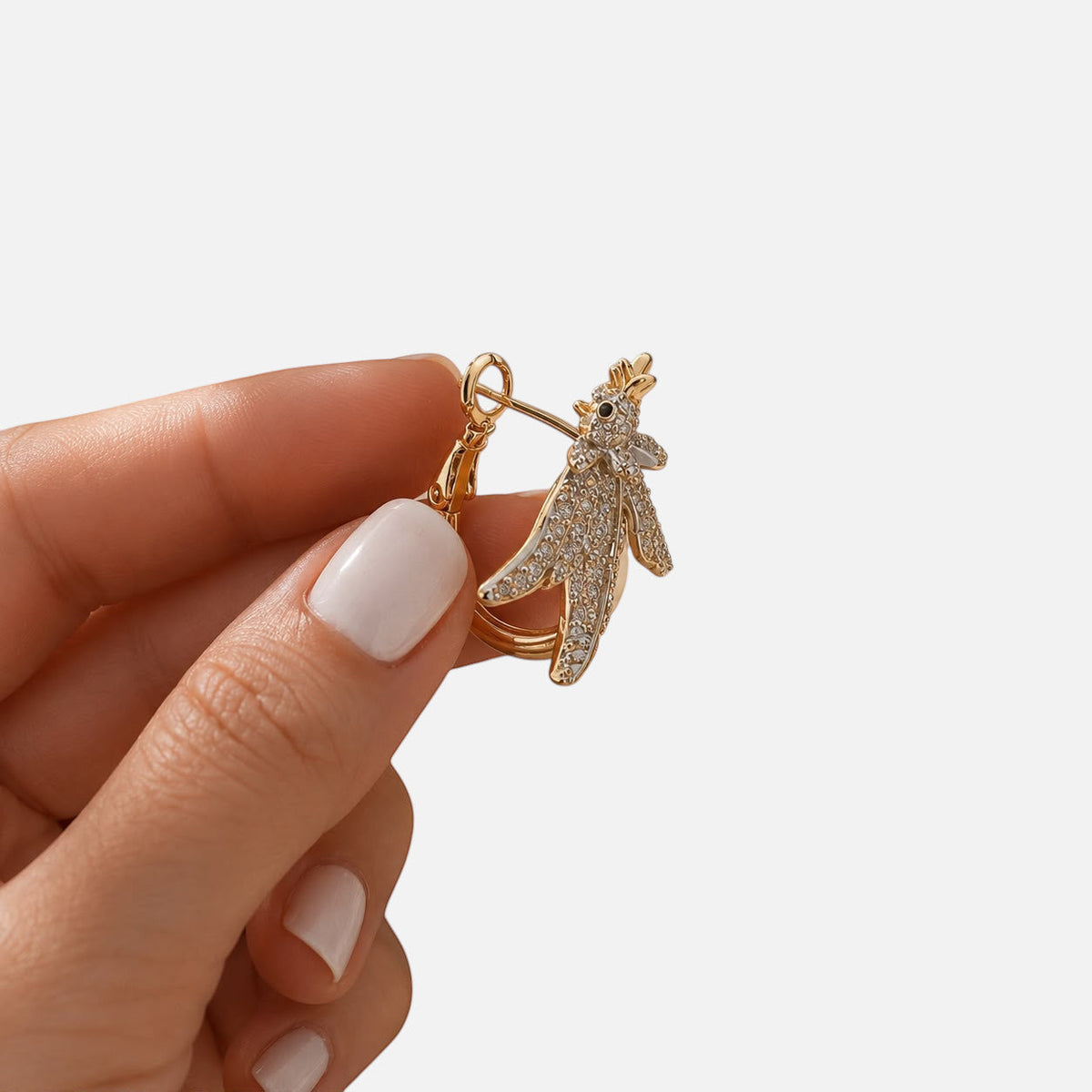Jakris gold hoop earring featuring a sparkling zircon-encrusted phoenix design held between fingers