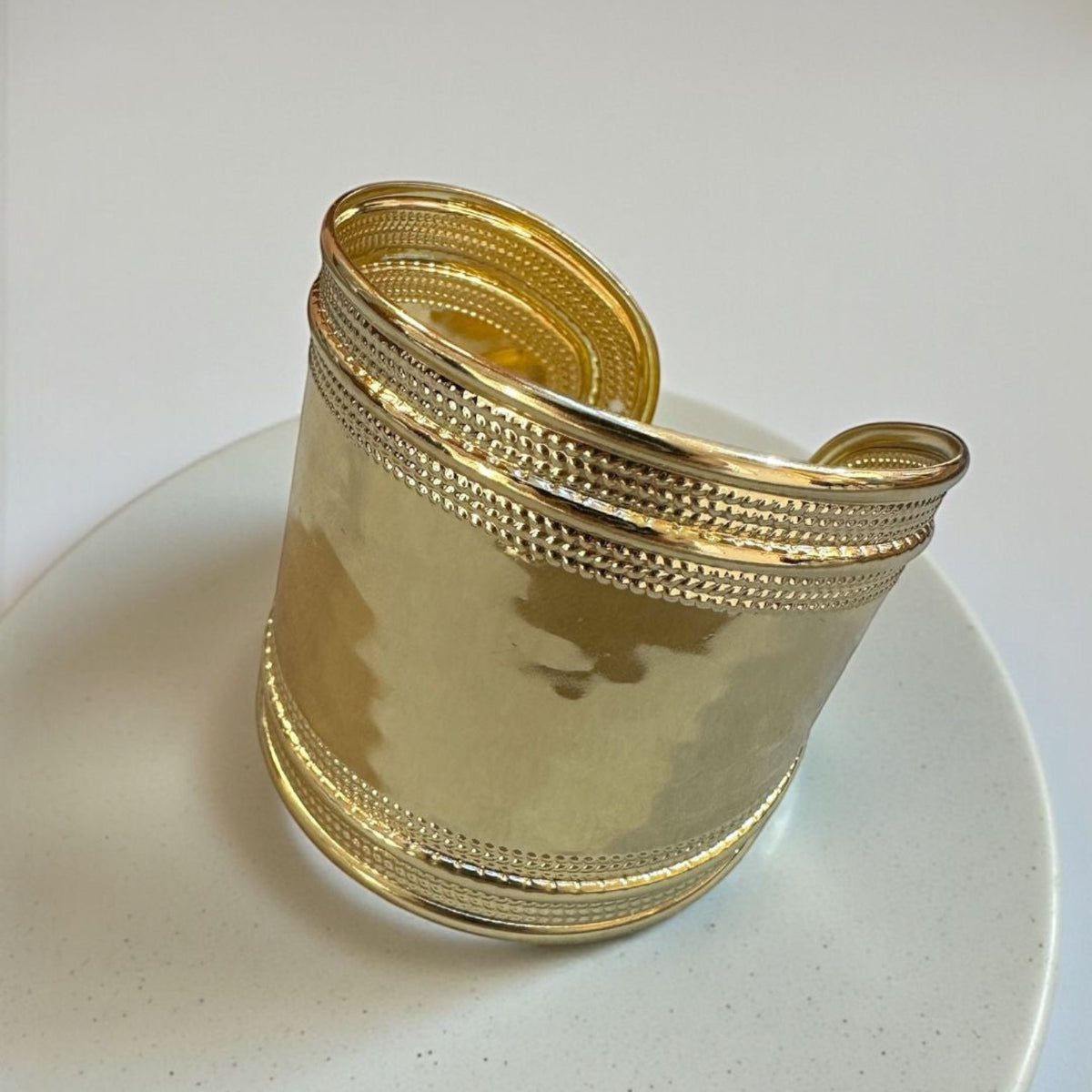 Jakris gold-plated brass cuff bracelet with a wide, textured, and polished finish on a white display stand.
