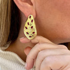Jakris gold-plated drop earrings featuring a textured organic shape and inlaid red ruby stones worn on an earlobe.