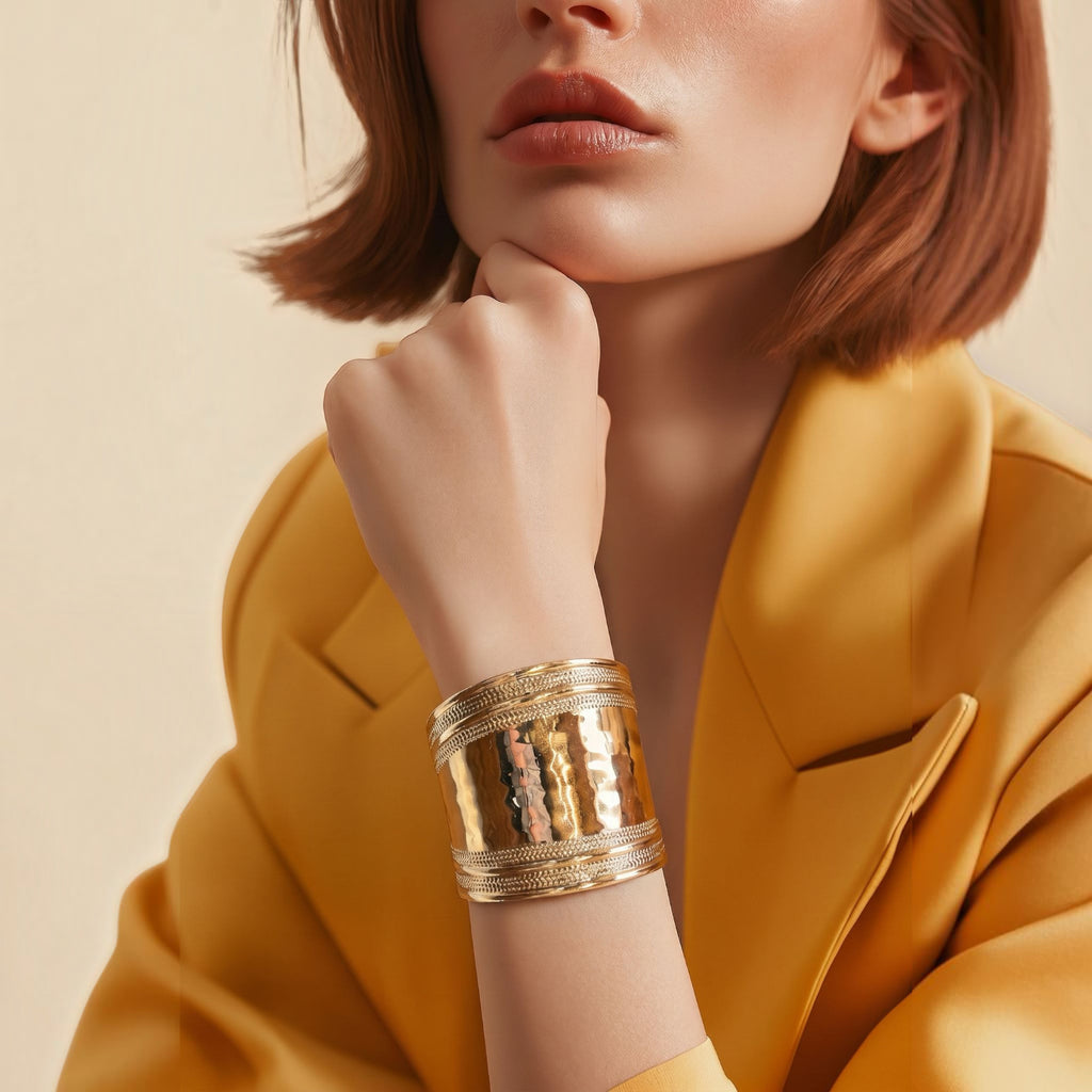 Jakris gold-plated brass cuff bracelet with a wide, textured, and shiny surface worn on a woman's wrist.