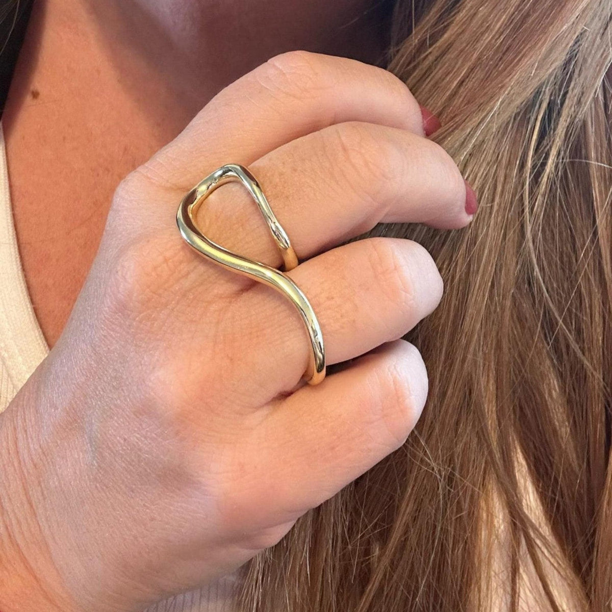Jakris gold-plated two-finger ring with a modern sculptural wave design worn on a hand
