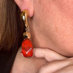 Jakris gold-tone drop earrings featuring a bold red marbled stone and polished metal accents worn on an earlobe.